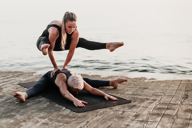 Caber mulher desportiva fazendo parada de mãos em acro yoga asana na praia perto do mar