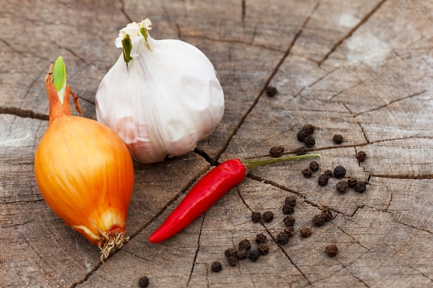 Una cabeza de cebolla de ajo y pimiento rojo picante en un primer plano de fondo de tocón de madera agrietada en un sol ...