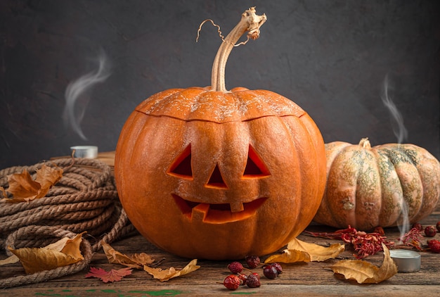 Foto cabeza de gato de calabaza de halloween sobre un fondo oscuro con follaje y velas apagadas