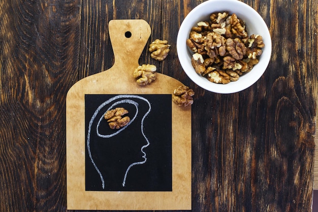 Cabeza de persona dibujada con cerebro y nueces nueces sobre fondo de madera