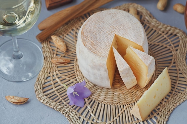 Una cabeza de queso fresco ecológico acompañada de pan, frutos secos, vino blanco y flores de verano. Concepto de comida sana y orgánica.