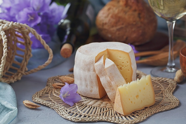 Una cabeza de queso fresco ecológico acompañada de pan, frutos secos, vino blanco y flores de verano. Concepto de comida sana y orgánica.