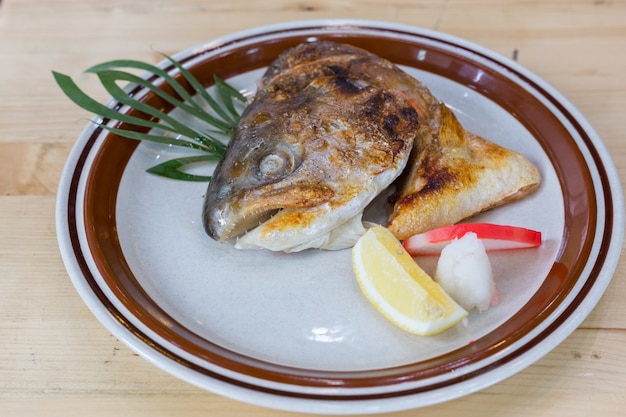 Cabeza de sal a la parrilla servida con limones en un plato blanco.