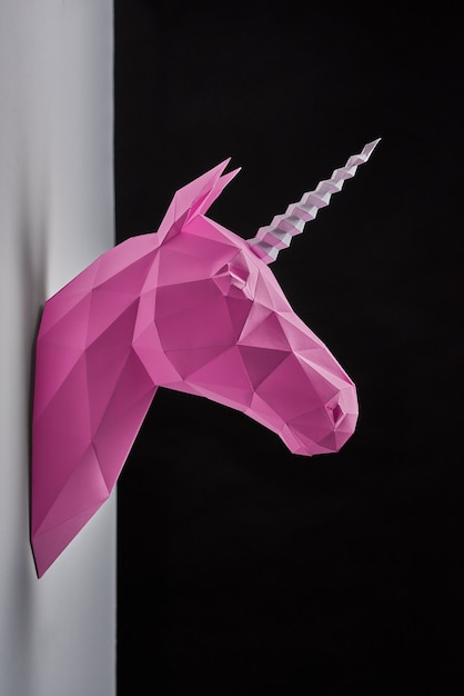 La cabeza de unicornio de color rosa pálido, hecha de papel colgando en la pared gris.