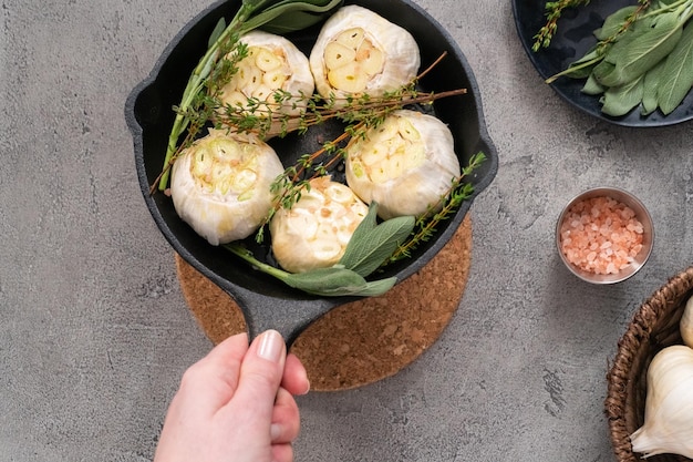 Cabezas de ajo crudo con especias frescas en sartén de hierro fundido para preparar la receta de ajo asado.