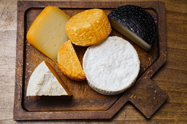 Cabezas de queso surtido sobre una tabla para cortar sobre una mesa de madera. quesería y quesería.