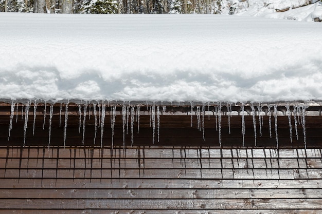 Cabine de madeira com telhado de neve e pingentes no dia ensolarado de inverno close-up