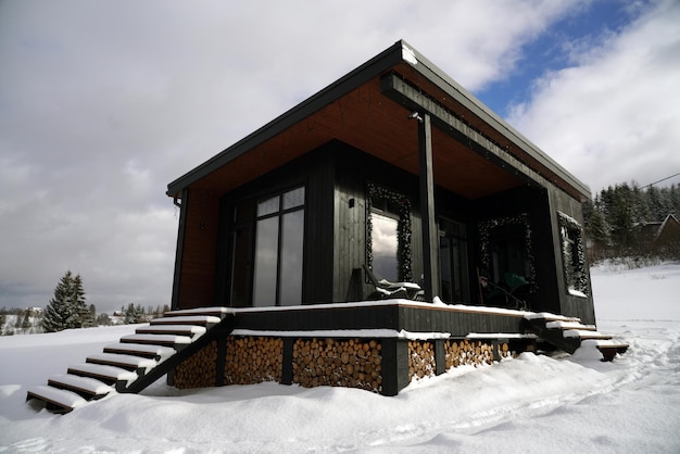 Foto cabine minúscula preta moderna em clima de neve com lenha empilhada sob