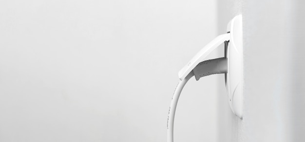 Cable enchufado en una toma de corriente blanca en una pared blanca en un interior moderno, diseño de banner con espacio para copiar