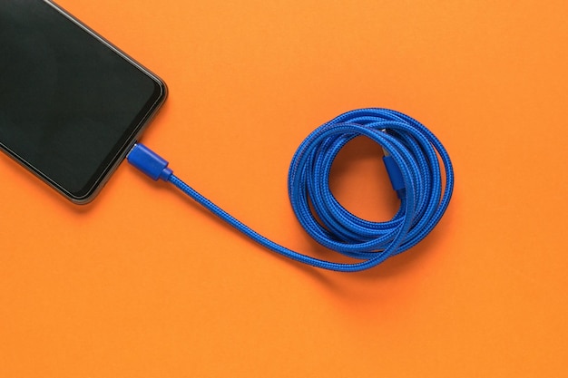 Cable USB azul y teléfono inteligente sobre un fondo naranja Lay Flat