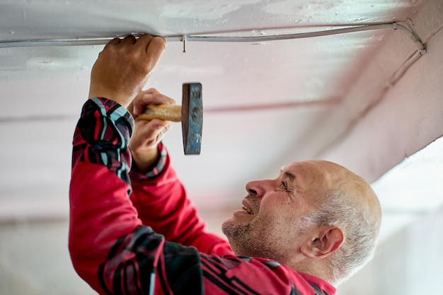 Foto cableado eléctrico externo en proceso de reparación de casa rural un anciano clavando alambre con