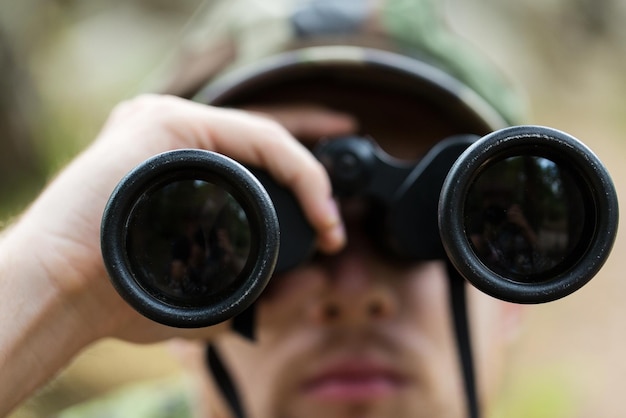 caça, guerra, exército e conceito de pessoas - close-up de jovem soldado, guarda florestal ou caçador com floresta de observação binocular