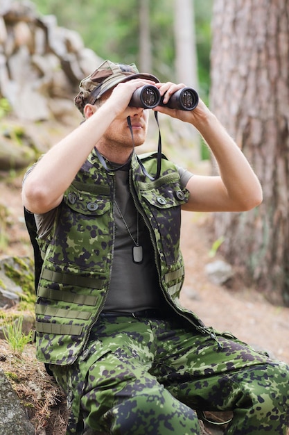 caça, guerra, exército e conceito de pessoas - jovem soldado, guarda florestal ou caçador com floresta de observação binocular