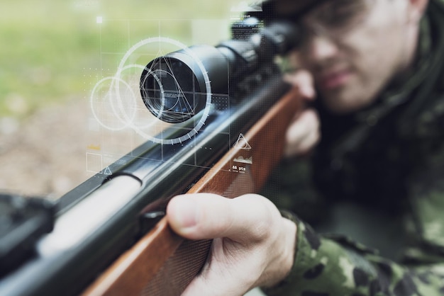 caça, guerra, exército, tecnologia e conceito de pessoas - close-up de jovem soldado ou atirador segurando arma com projeção de tela virtual e mirando na floresta