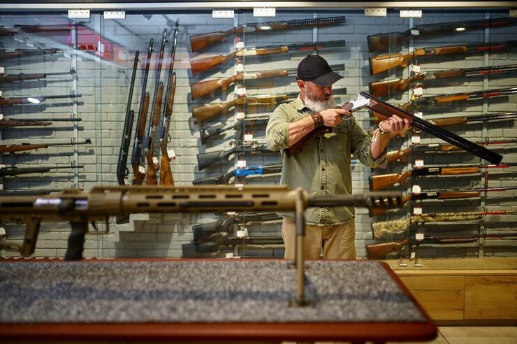 Foto caçador barbudo verifica o rifle de caça na loja de armas. interior da loja de armas, variedade de munições e munições, escolha de armas de fogo, hobby de tiro e estilo de vida