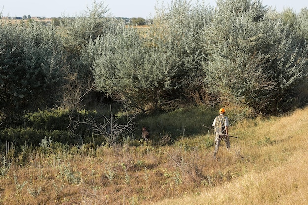 Caçador de patos com espingarda andando por um prado xarvista de um homem com uma arma nas mãos