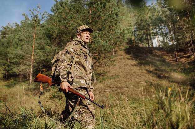 Caçador em roupas de camuflagem pronto para caçar com rifle de caça