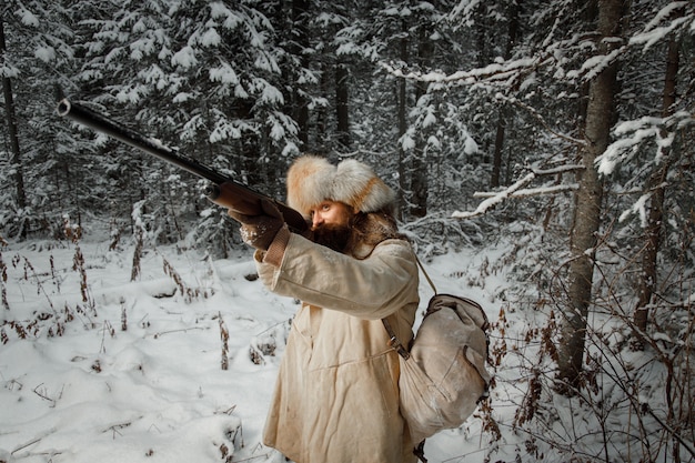 Caçador em roupas vintage com arma foge pela floresta