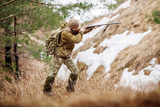 Caçador feminino em roupas de camuflagem pronta para caçar segurando arma e andando na floresta