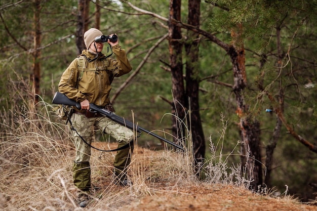 Caçador feminino em roupas de camuflagem pronta para caçar segurando arma e andando na floresta