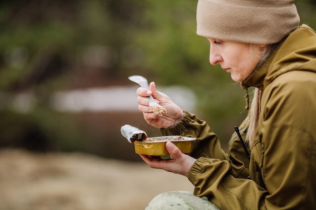 Caçador feminino preparando comida com um queimador de gás portátil em uma floresta de inverno