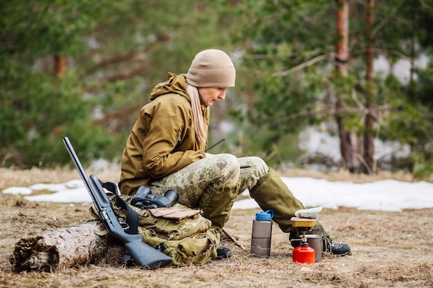 Caçador feminino preparando comida com um queimador de gás portátil em uma floresta de inverno