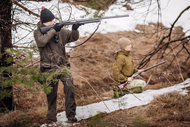 Caçador masculino com binóculos pronto para caçar segurando arma e andando na floresta