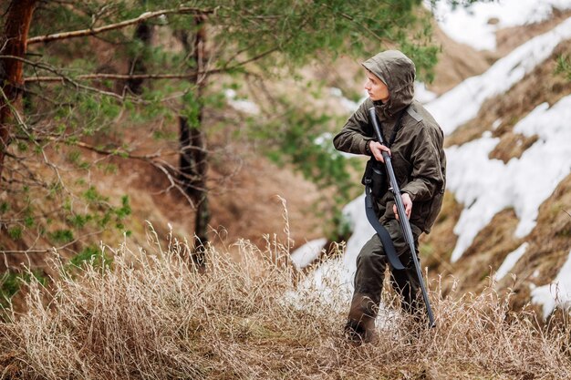 Caçador masculino com binóculos pronto para caçar segurando arma e andando na floresta