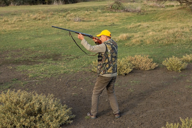 Caçador mirando com rifle em pé contra o céu