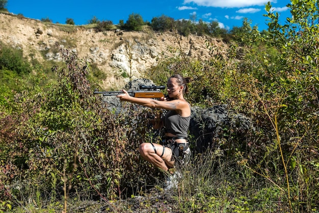 Caçador sexy com rifle posando no horário de verão ao ar livre