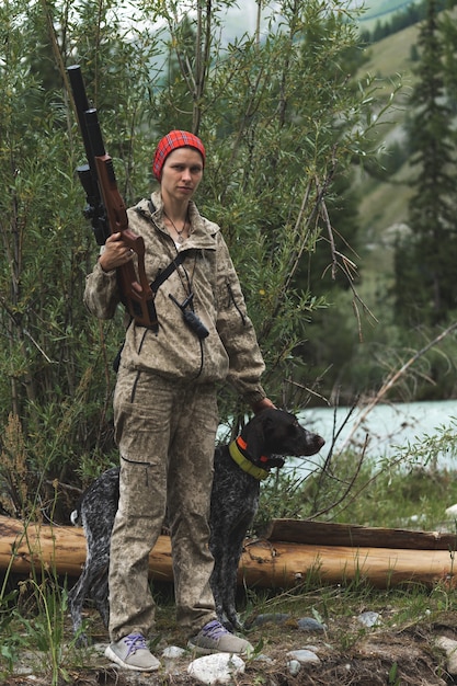 Caçadora feminina com roupas de camuflagem, pronta para caçar, segurando uma arma e caminhando na floresta. conceito de caça e pessoas