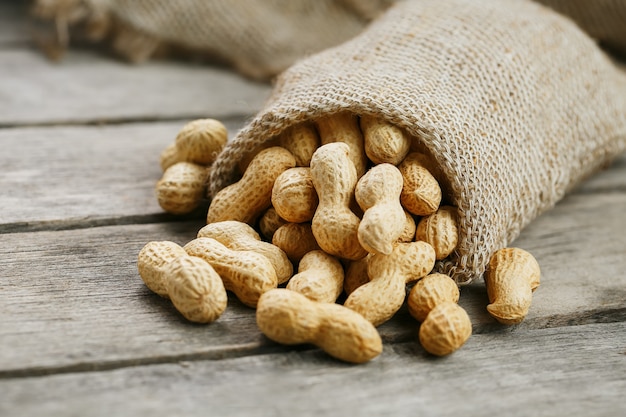 Cacahuetes en una bolsa de arpillera en miniatura sobre una superficie de madera vieja y gris