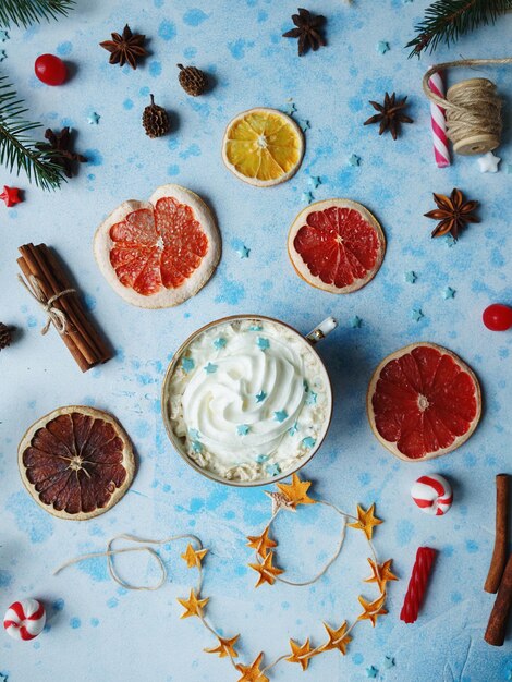 Foto cacao casero o chocolate caliente con crema de naranjas secas, caramelos de canela de abeto y nueces sobre fondo de hormigón azul. bebida de navidad o año nuevo, decoración casera acogedora, vista superior, enfoque selectivo.