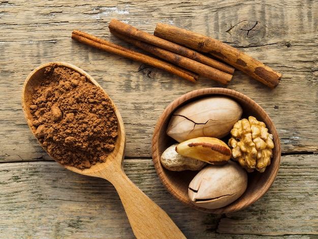 Cacao en una cuchara de madera y nueces sobre una mesa de madera.