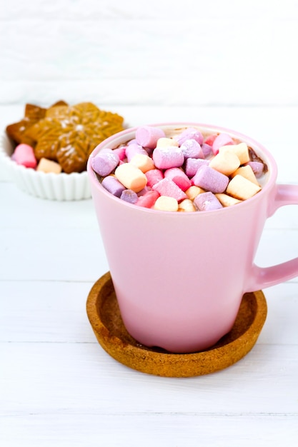 Cacao navideño con malvavisco en una taza rosa y galleta de jengibre sobre una mesa de madera