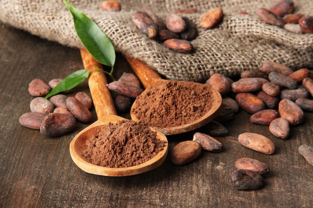 Cacao en polvo en cucharas y granos de cacao sobre fondo de madera