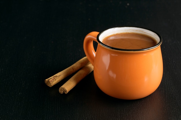 Cacao en una taza anaranjada en un fondo negro.