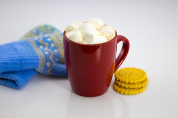 Cacao en taza roja con malvaviscos y galletas, aislado sobre fondo blanco.