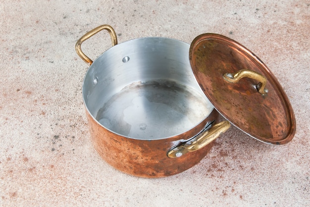 Foto caçarola de cobre velha com tampa e alças de latão em uma mesa de concreto.