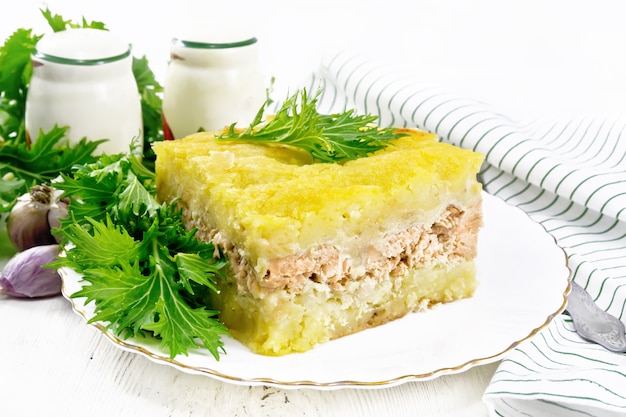 Caçarola de purê de batata com filé de salmão e alface em um prato, pano de prato, alho no fundo de uma placa de madeira leve