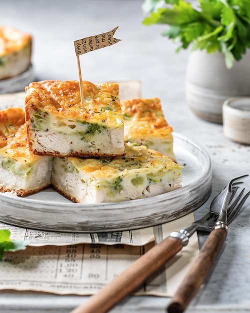 Caçarola fatiada de queijo brócolis de frango em um prato com talheres em fundo cinza Comida saudável