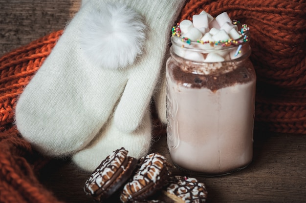 Cacau com marshmallows, biscoitos de chocolate, cachecol laranja de malha e luvas brancas