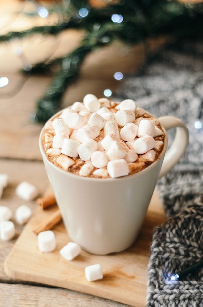 Cacau quente com marshmallow e especiarias na mesa de madeira com uma manta de malha cinza.