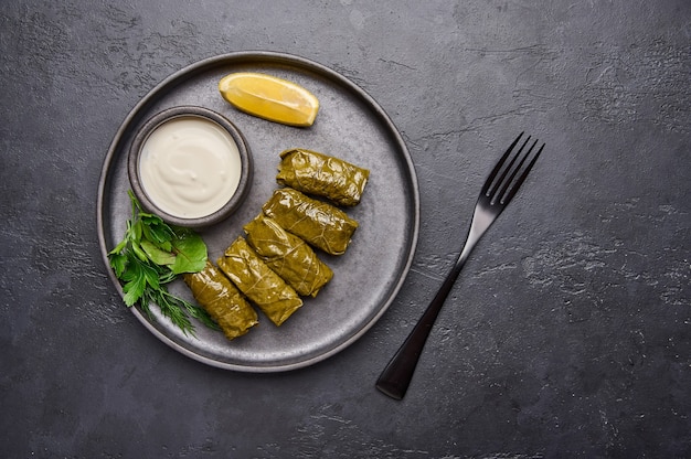 Cacerola de perejil dolma con crema agria y limón en placa negra sobre una mesa oscura cerca de la parte superior de la horquilla negra