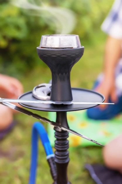 Cachimbo de água com brasas fumegantes, as pessoas estão sentadas em volta do cachimbo de água e fumando-o ao ar livre