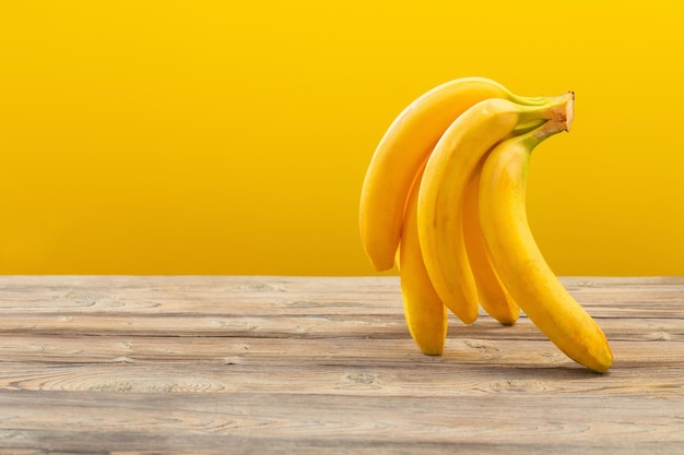 Cacho de bananas na mesa de madeira no fundo amarelo