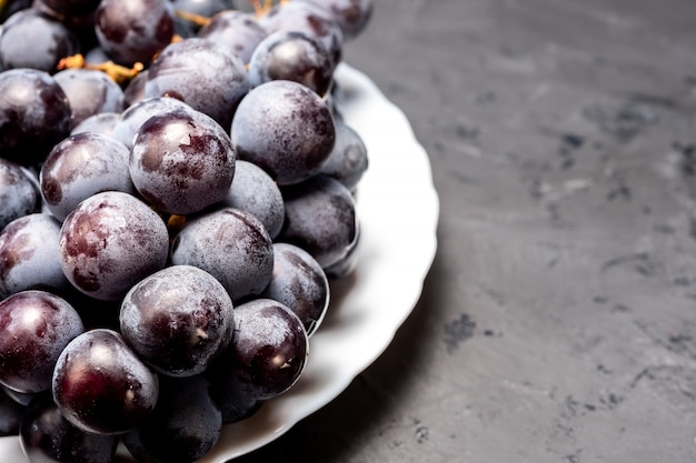 Cacho de uvas maduras pretas em um prato branco