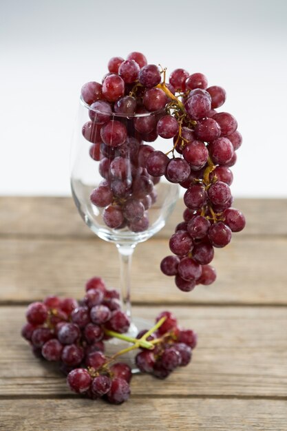 Cacho de uvas vermelhas em uma taça de vinho na mesa de madeira