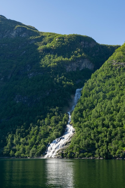 Cachoeira no fiorde de Geiranger cercada por árvores verdes e altas montanhas na Noruega