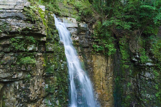 Cachoeira no rio da montanha com água espumosa branca caindo de formação rochosa na floresta de verão.